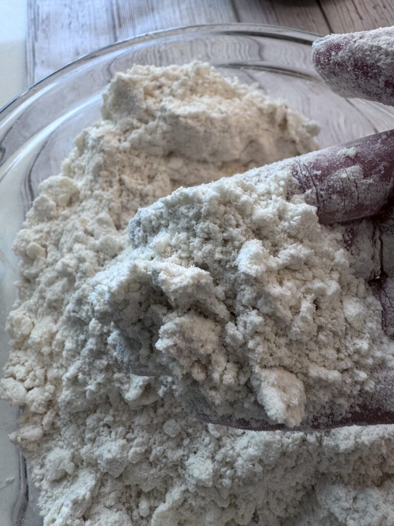 Using the slicing side of a box grater, slice the butter into the flour mixture. Toss the sheets of butter in the flour and then lightly work the butter pieces between your fingers, or use a pastry cutter to break them up and coat them with flour. Stop when the dough resembles coarse sand, and there are still some small visible pieces of butter.