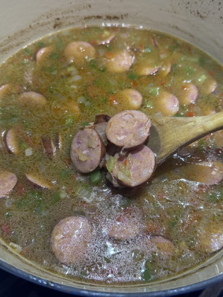 1. Add the sliced andouille sausage and minced garlic to the pot. Reduce the heat to low and let the gumbo simmer uncovered for about 45 minutes, stirring occasionally to prevent sticking.